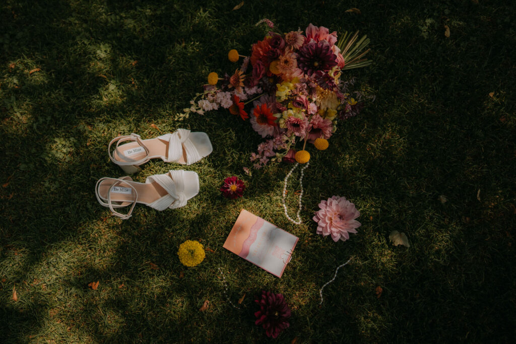 Flatlay von oben mit Brautschuhen und Blumenstrauß im Gras bei der Hochzeit auf Schloss Ottersbach