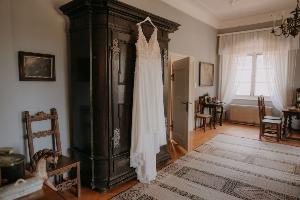 Brautkleid hängt an einem antiken Holzkasten im Ankleidezimmer auf Schloss Ottersbach