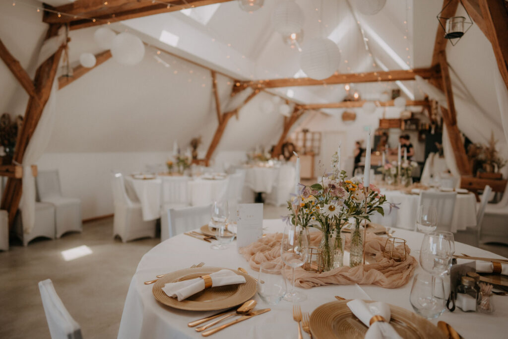 Festlich gedeckte Hochzeitstafel unter Holzbalken im Scheunengebäude – Obstbau Haas