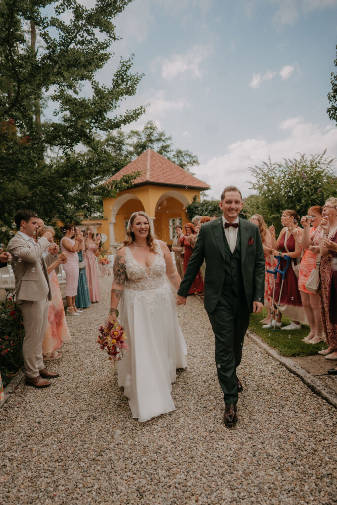 Brautpaar geht Hand in Hand den Kiesweg entlang bei der Hochzeit auf Schloss Ottersbach, im Hintergrund der Pavillon
