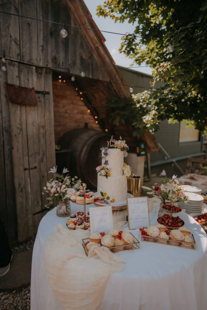 Zweistöckige Hochzeitstorte mit frischen Blüten am Dessertbuffet vor rustikaler Scheune beim Obstbau Haas