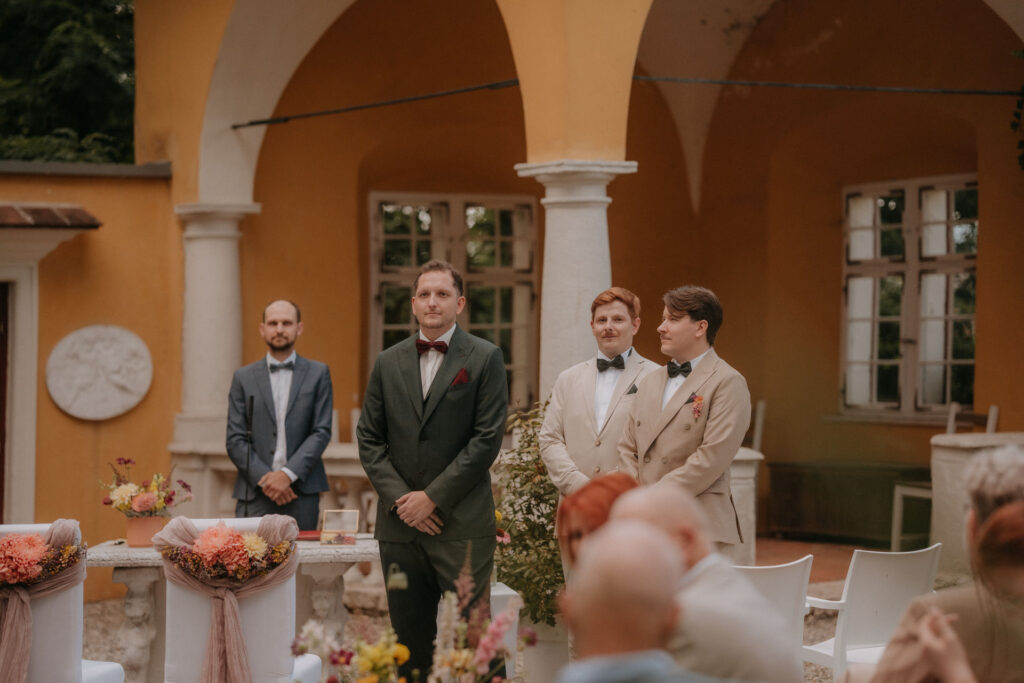 Trauzeugen und Gäste warten unter dem Arkadengang auf die Braut bei der Hochzeit auf Schloss Ottersbach