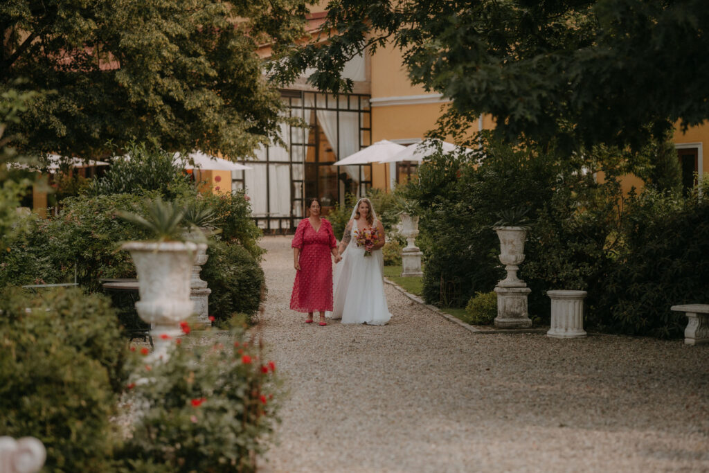 Braut geht Hand in Hand mit ihrer Mutter den Kiesweg entlang zur Trauung auf Schloss Ottersbach