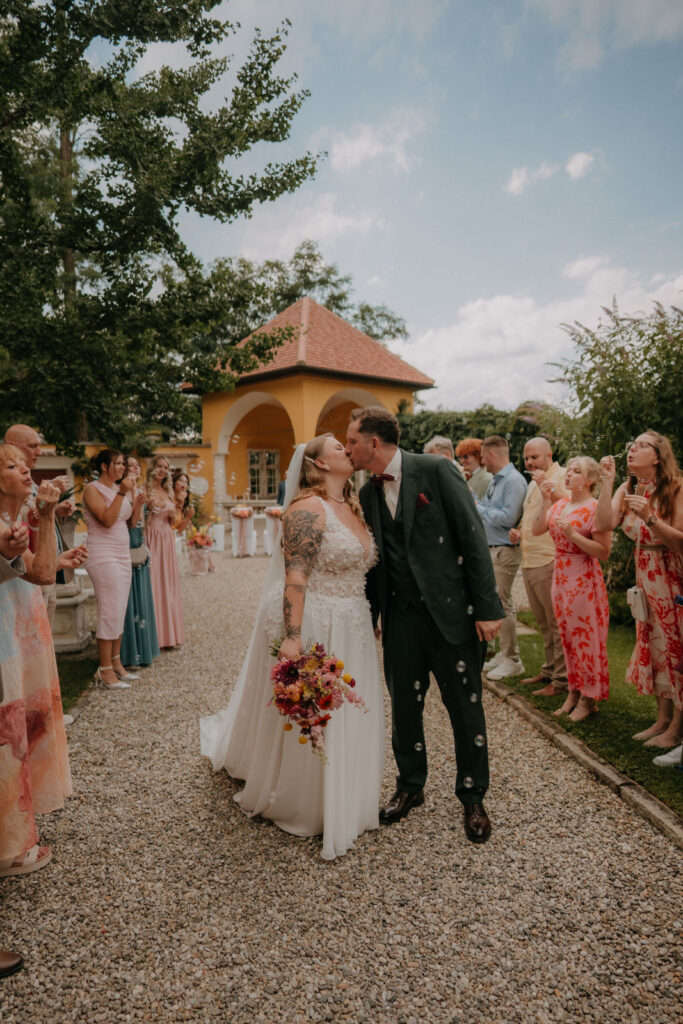 Brautpaar küsst sich unter Konfettiregen der jubelnden Gäste bei der Hochzeit auf Schloss Ottersbach