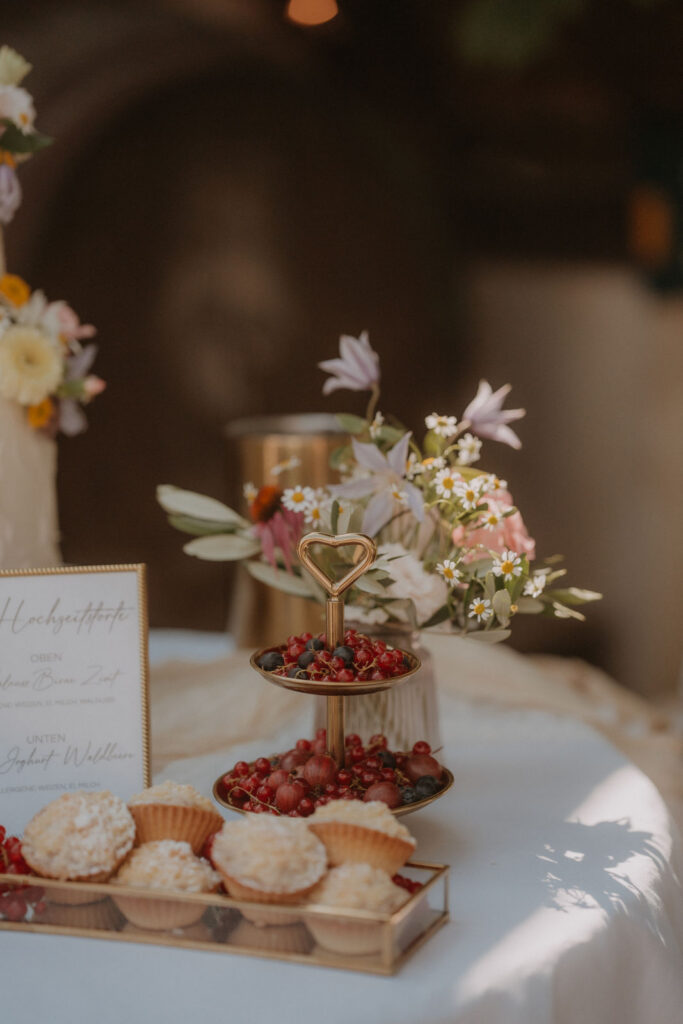 Herzförmiger Etagenteller mit Beeren und Cupcakes neben der Hochzeitstorte