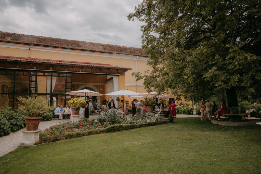 Hochzeitsgäste feiern unter Sonnenschirmen auf der Terrasse von Schloss Ottersbach