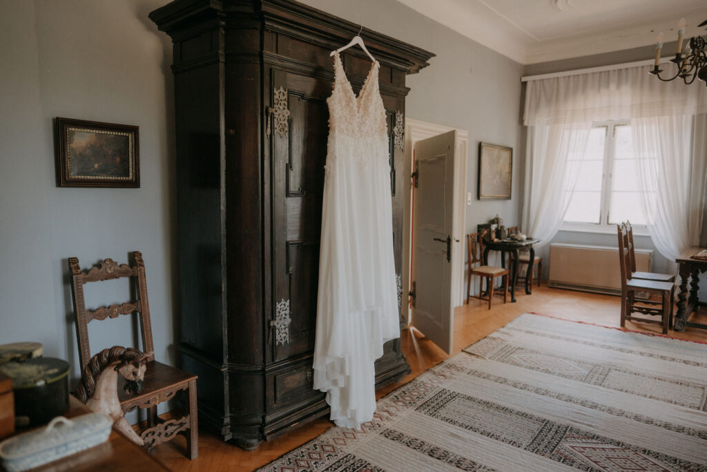Brautkleid hängt an einem antiken Holzkasten im Ankleidezimmer auf Schloss Ottersbach