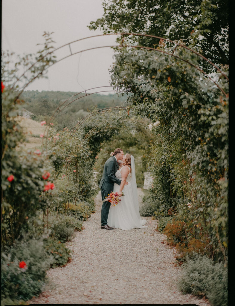 Analog fotografierter Kuss von Braut und Bräutigam unter dem Rosenbogen auf Schloss Ottersbach
