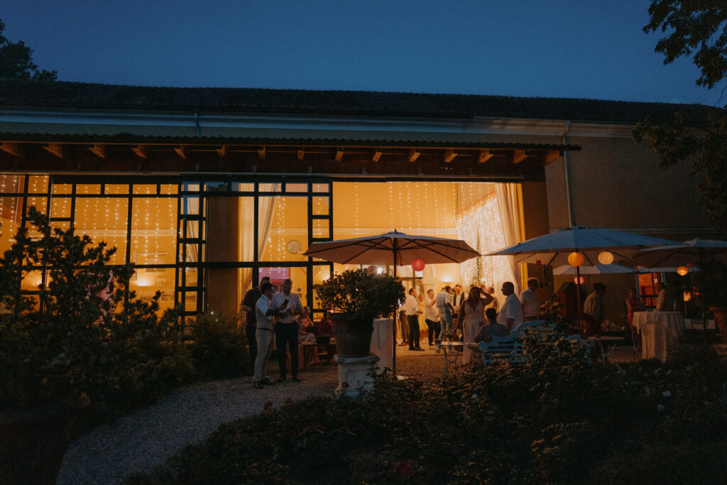 Beleuchtete Terrasse von Schloss Ottersbach bei Nacht mit feiernden Hochzeitsgästen unter Lichterketten