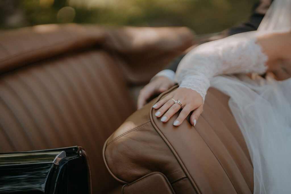 Hand der Braut mit Ehering auf dem Ledersitz des Oldtimers